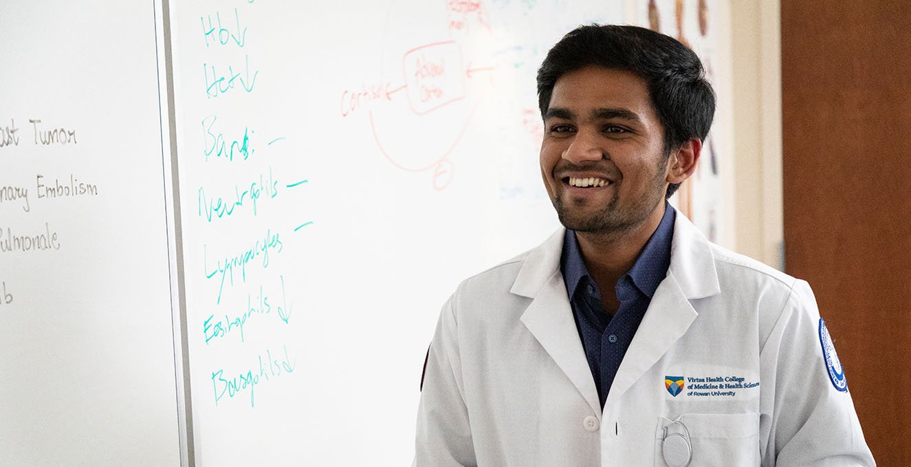 An SOM student smiles in a classroom next to a white board.