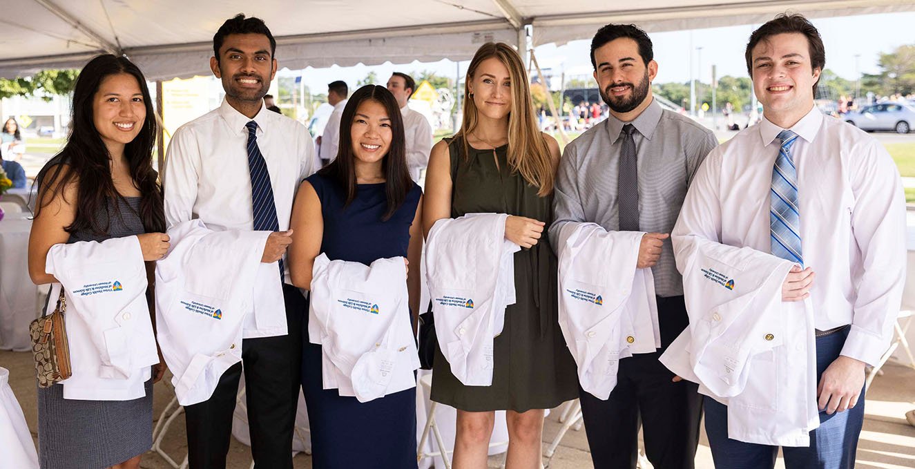 a group of smiling SOM students hold their white coats at the white coat ceremony