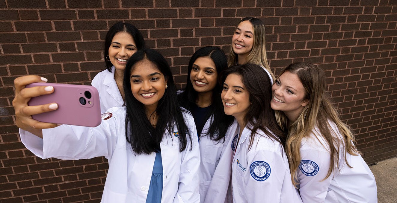 A group of smiling SOM students take a selfie at the white coat ceremony