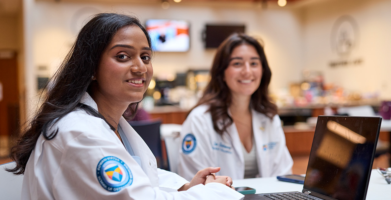 two med students smile while studying and talking at a table in the cafe at the Sewell campus