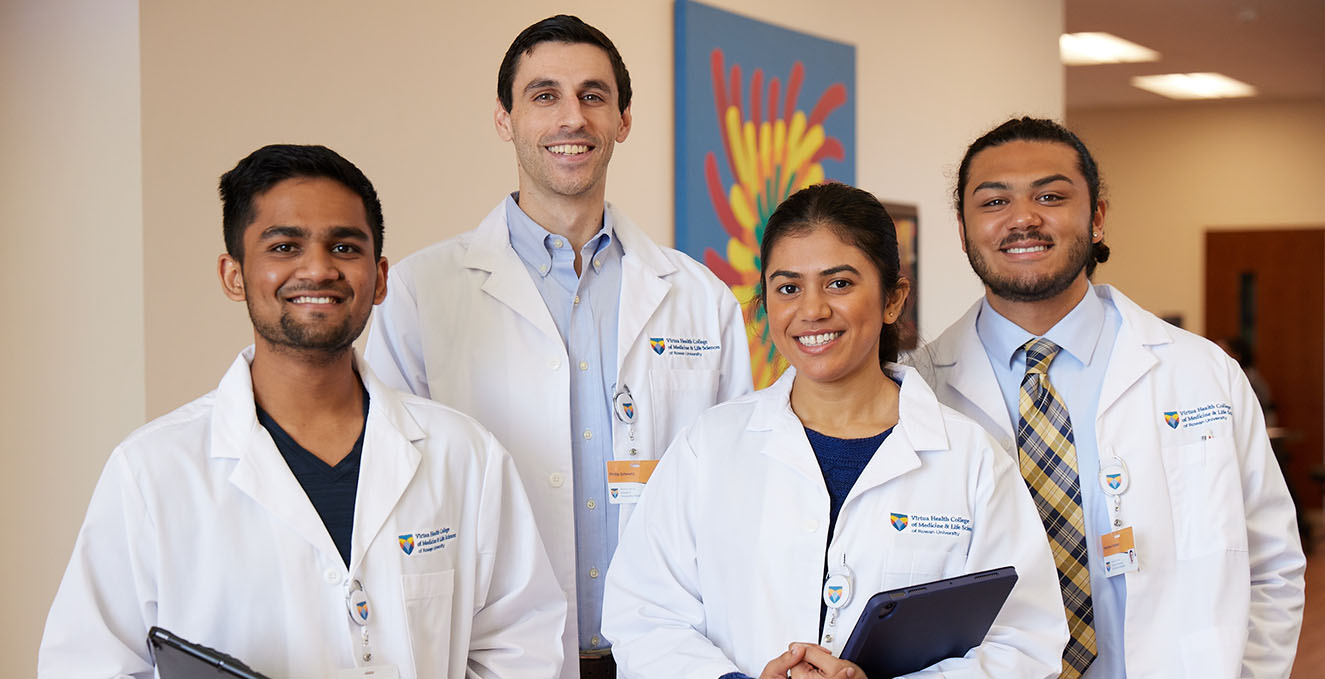 Four smiling SOM students stand in the hallway at the Sewell Rowan Medicine building