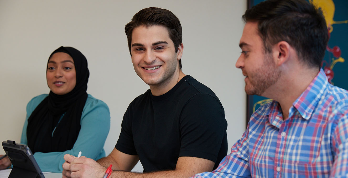 a smiling Rowan-Virtua SOM student looks at the camera while sitting at a table with other students