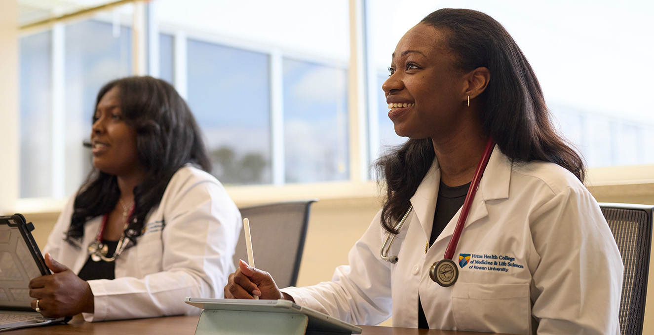 Two SOM students smile at a desk while in class