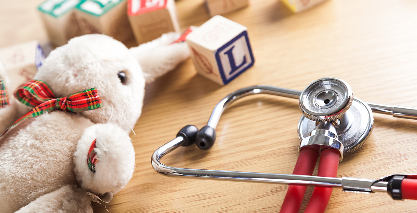 a beige stuffed bunny lies on a table with children's wooden blocks and a stethoscope