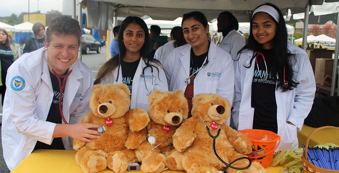 a group of SOM students listen to the heartbeat of a teddy bear
