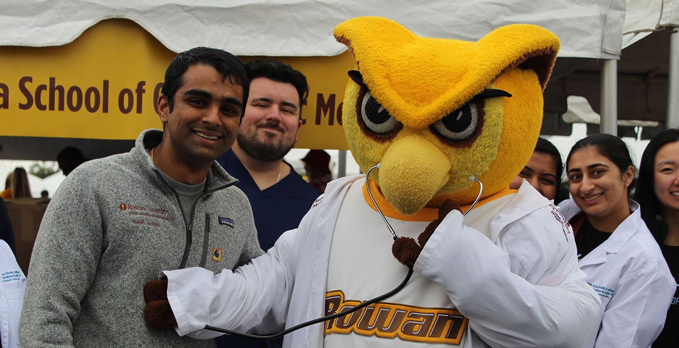 The Rowan mascot, Prof, listens to the heartbeat of a SOM student at homecoming