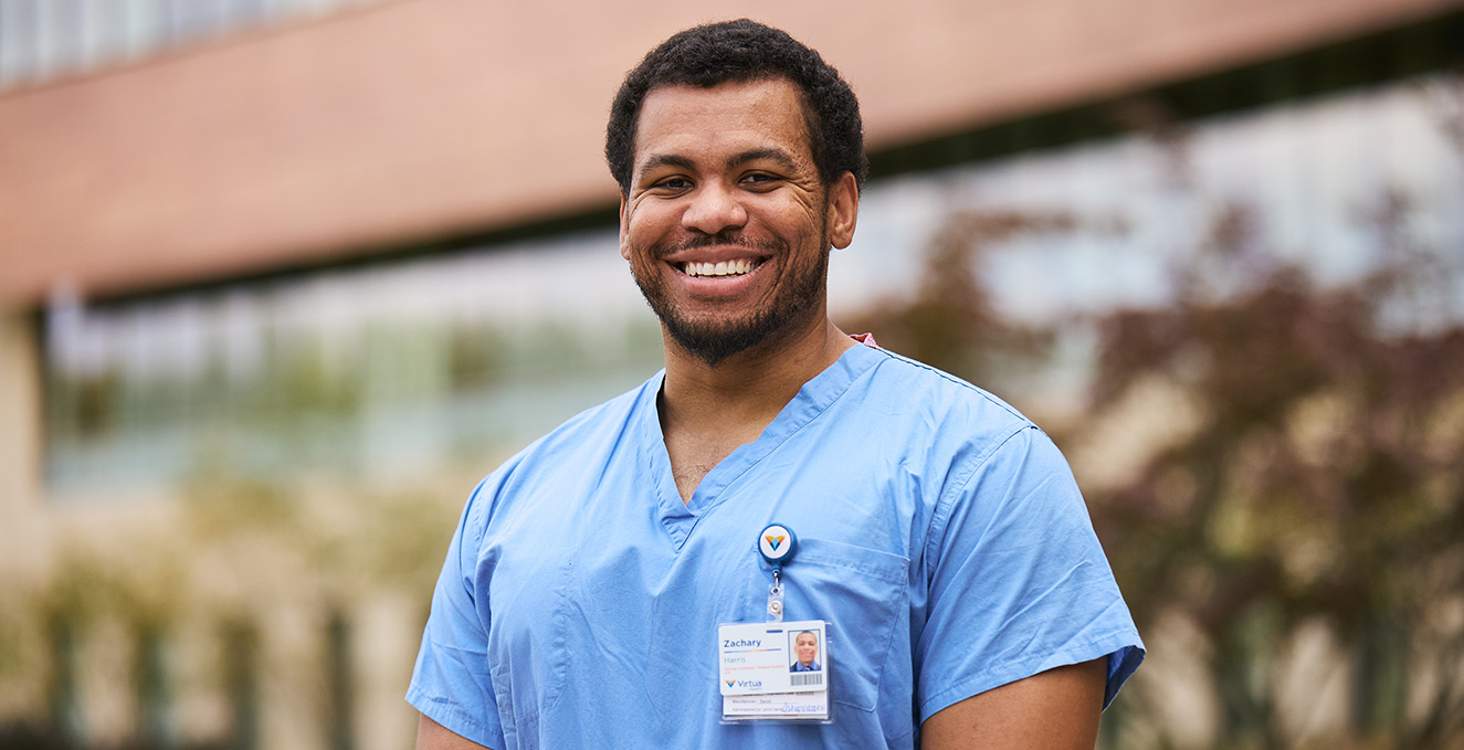 SOM medical student wearing blue scrubs and a Virtua hospital badge smiles while standing outside Virtua Voorhees hospital 