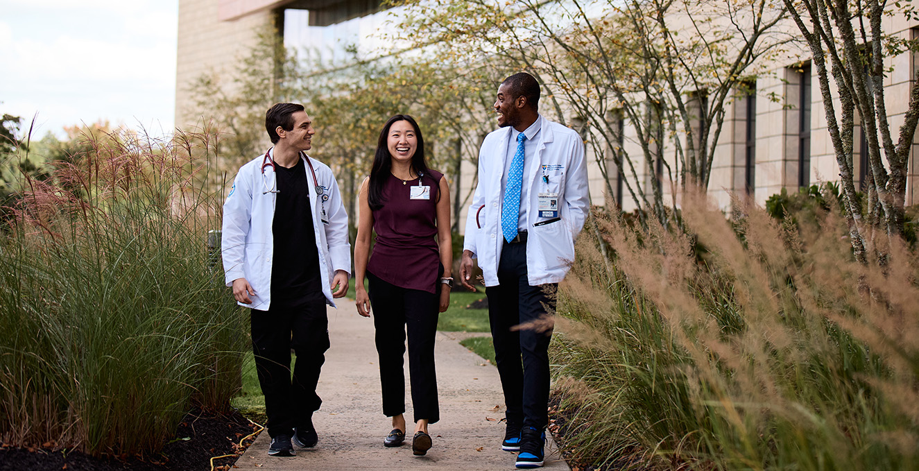 three SOM medical students walk while talking and laughing on the sidewalk outside the Virtua Voorhees hospital