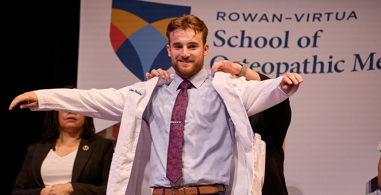 A Rowan-Virtua SOM medical student puts on his white coat at the white coat ceremony