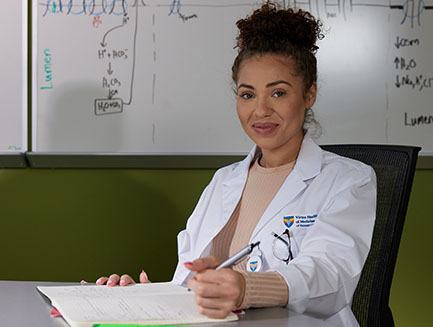 smiling female SOM student sits at a desk with a white board behind her