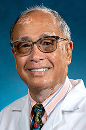 Kai Mon Lee smiles for the camera while wearing his glasses, a white lab coat, a striped shirt, and patterned tie