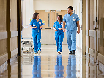 three doctors in blue scrubs walk down a hospital hallway