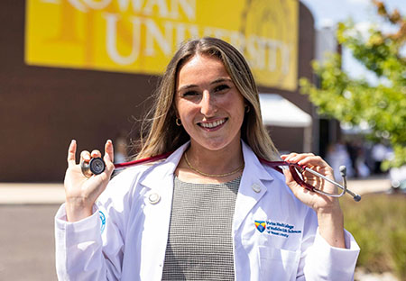 a medical student stands outside the auditorium holding a stethoscope