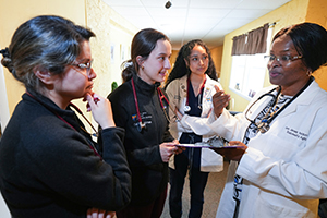 two SOM medical students listen as two physicians explain something while standing in a clinic during a community service event