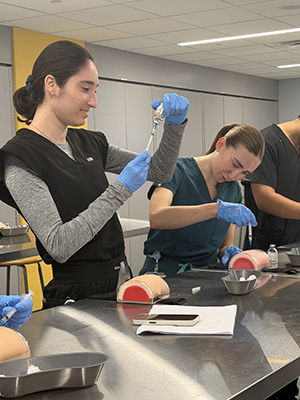 a student draws a syringe while another student practices next to her in the skills lab