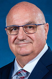 David Condoluci smiles for the camera while wearing a blue suit jacket, red and blue patterned tie, and a white button down