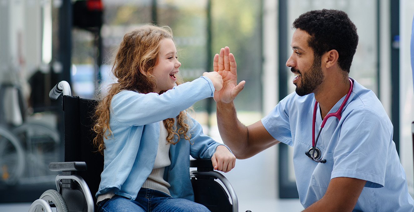 a health care worker squats down and high fives a child in a wheel chair