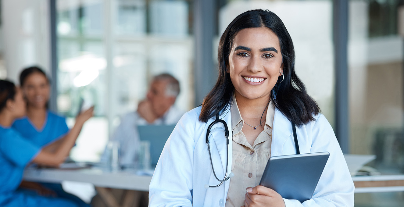 a smiling medical student holding a blue folder stands in a room