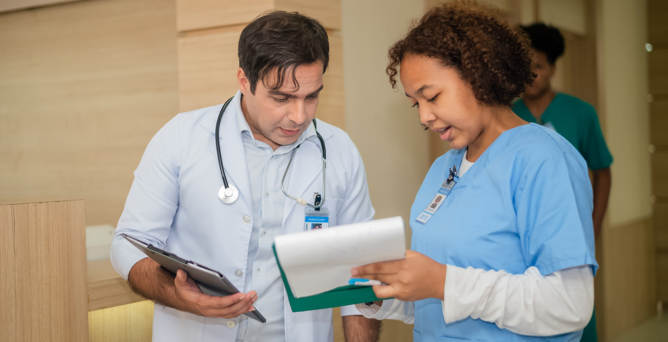 two health care workers talk over a document in the hallway