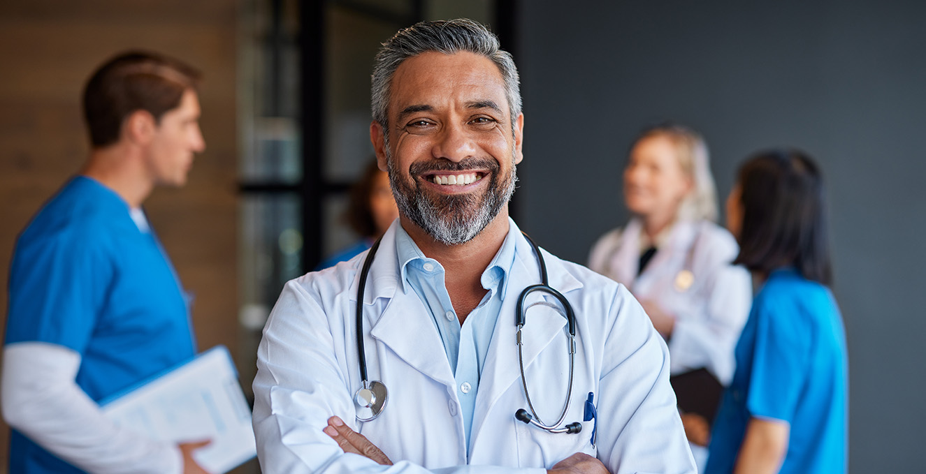 a male health care provider smiles into the camera while others talk in the background