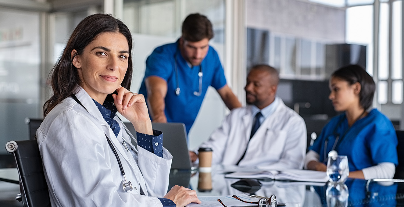 A smiling health care student sits at a table while other talk behind her