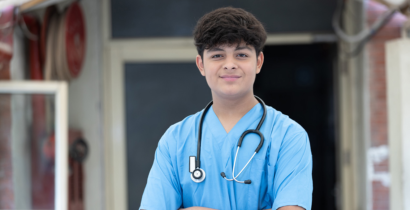 a male health care worker in scrubs with a stethoscope smiles at the camera