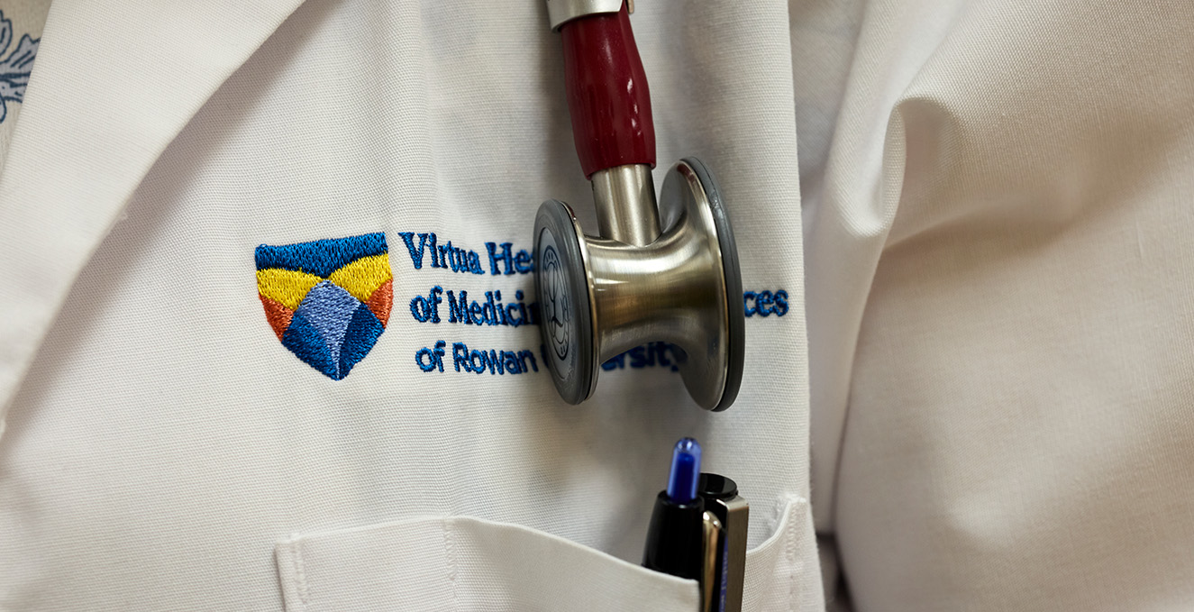 a stethoscope rests on the Virtua Health College logo on a white coat that has pens in the pocket