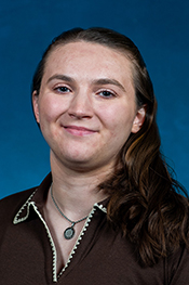 Emily Icaovone smiles at the camera, ponytail sitting to the side on a brown shirt