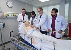 a mannequin on a stretcher is programmed with symptoms and med students discuss the case and work through treatments with stethoscope and case notes