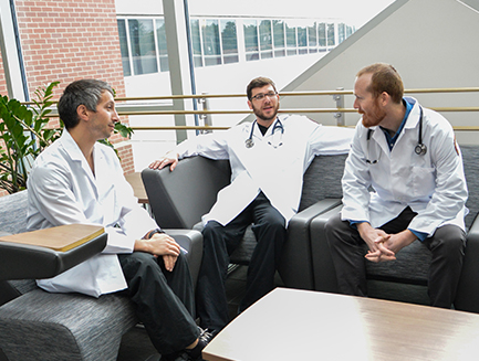 three smiling residents talk in the atrium of the Stratford Rowan Medicine building