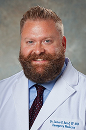 James Baird smiles at the camera while wearing a blue button-down, maroon tie, and his white coat