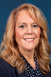 Pamela Basehore smiles at the camera while wearing a blue shirt with white polka dots and a blue jacket