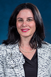 Alissa Brotman smiles at the camera while wearing a black and white suit jacket with a flower on the lapel