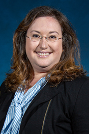 Anne Jones smiles at the camera while wearing a light blue blouse, dark blue jacket and her glasses