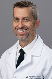 Kevin Overbeck smiles for the camera while wearing a tie and a white coat