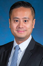 Timothy Wong smiles at the camera while wearing a white button-down, light blue tie and a dark blazer