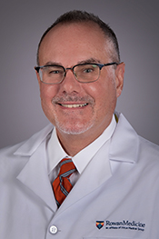 Dominck Zampino smiles for the camera while wearing a white button-down shirt, red tie and his white coat