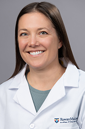 Clare Stpehens smiles at the camera while wearing a light blue shirt and whitecoat with the Rowan Medicine logo