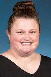 Megan Olsen smiles for the camera with her hair in a bun on top of her head and wearing a black, v-neck shirt