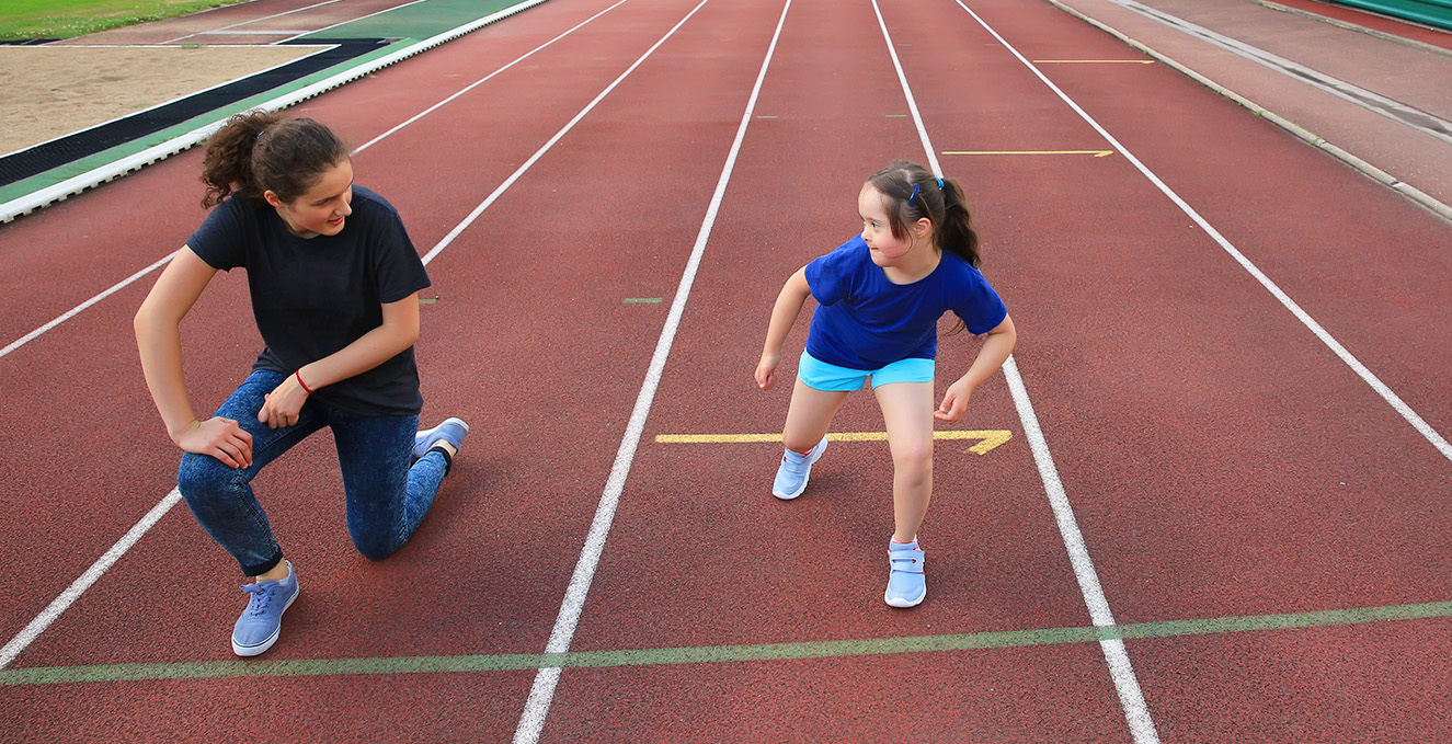 a female young adult stretches with a younger girl on a track