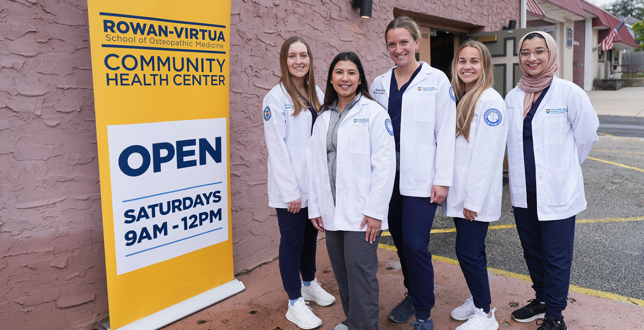 SOM medical students stand next to a sign that reads Rowan-Virtua SOM Community Health Center