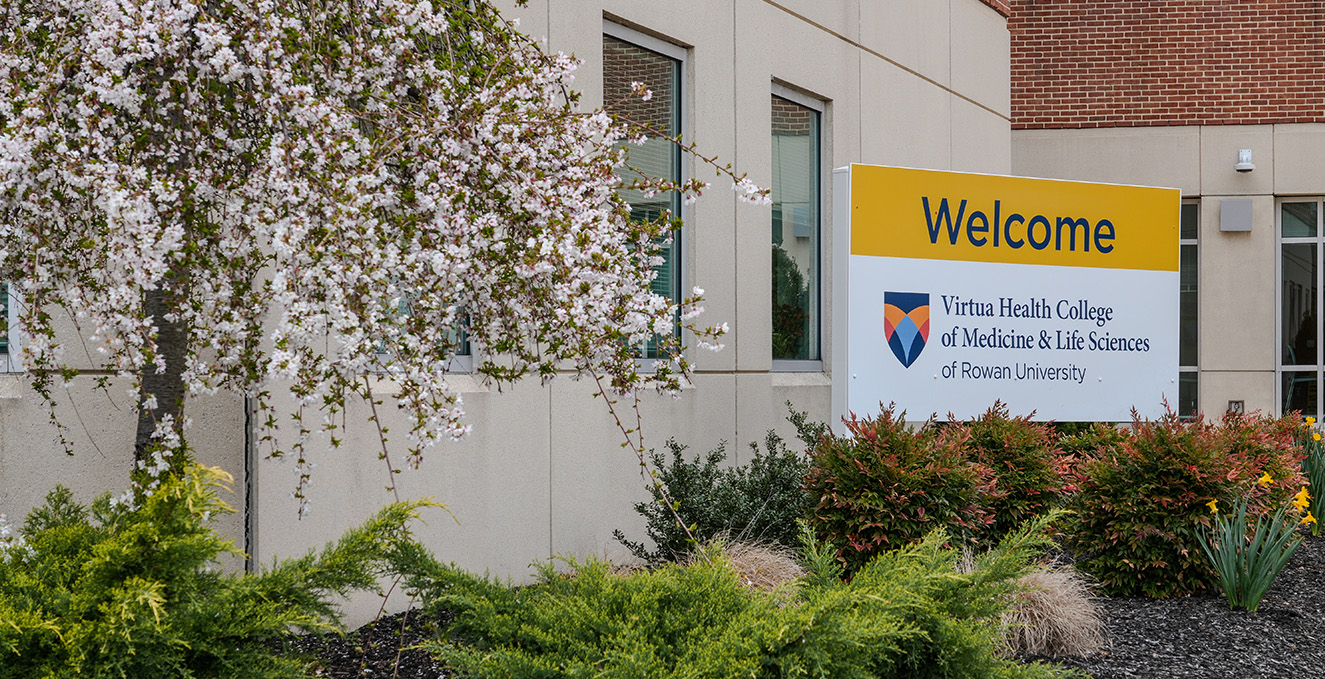 A welcome sign for Virtua health College in a flower bed with a blooming tree