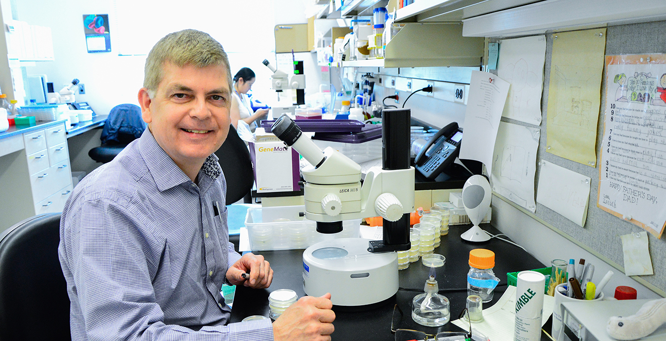 researcher smiling at a microscope