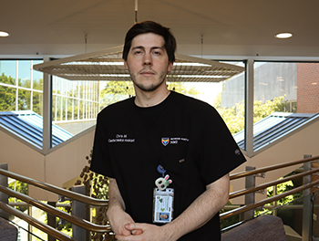 Christopher Marchione, wearing scrubs with a VHC logo, stands in the lobby of the Rowan Medicine building