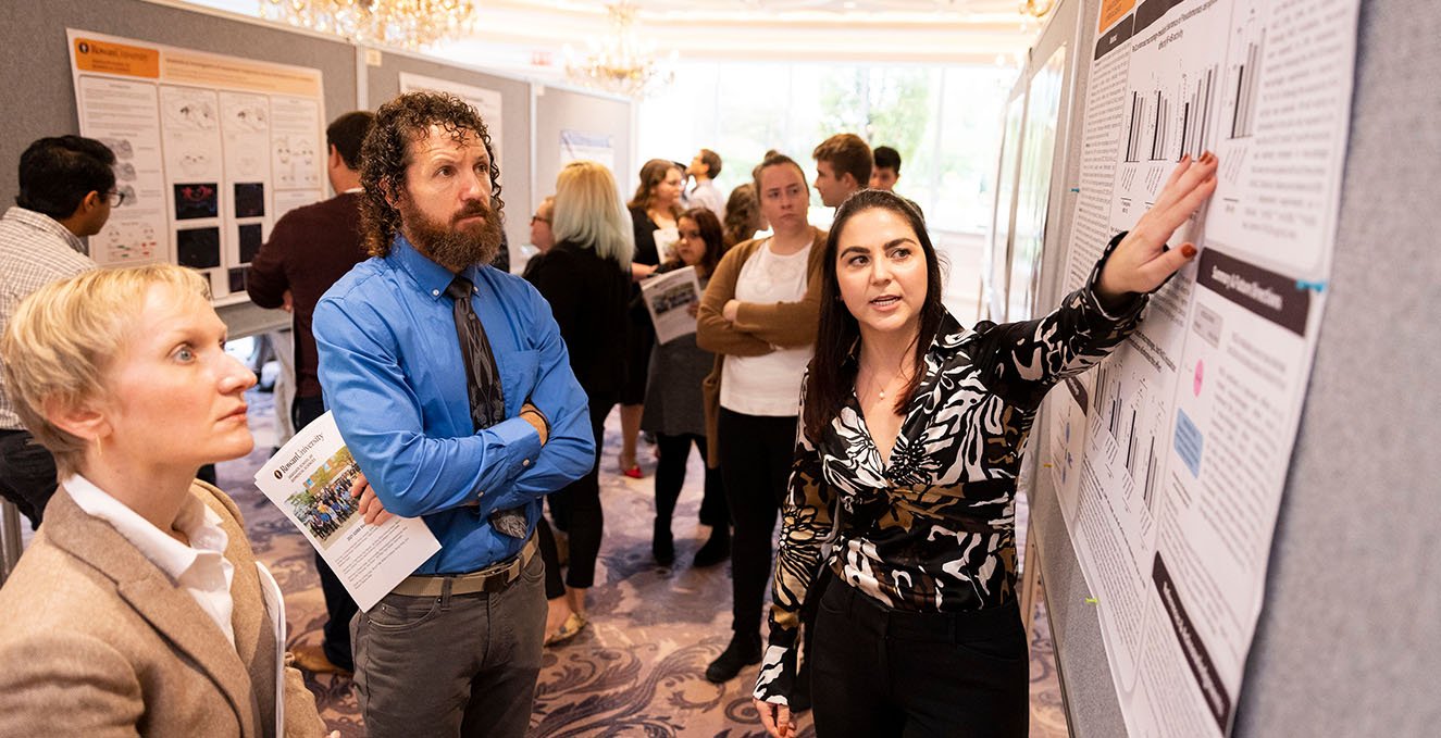 An SOM student discusses their research poster with two faculty members.