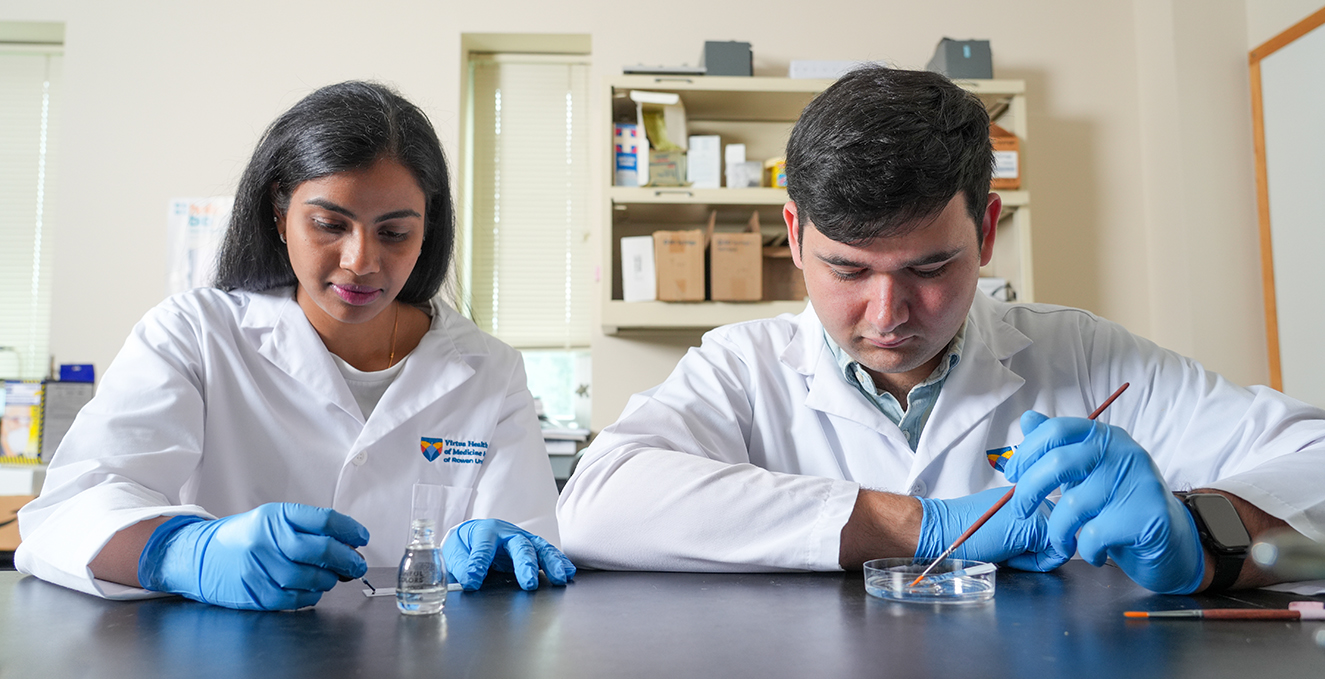 two research students working on slides and a dish at a table in the lab
