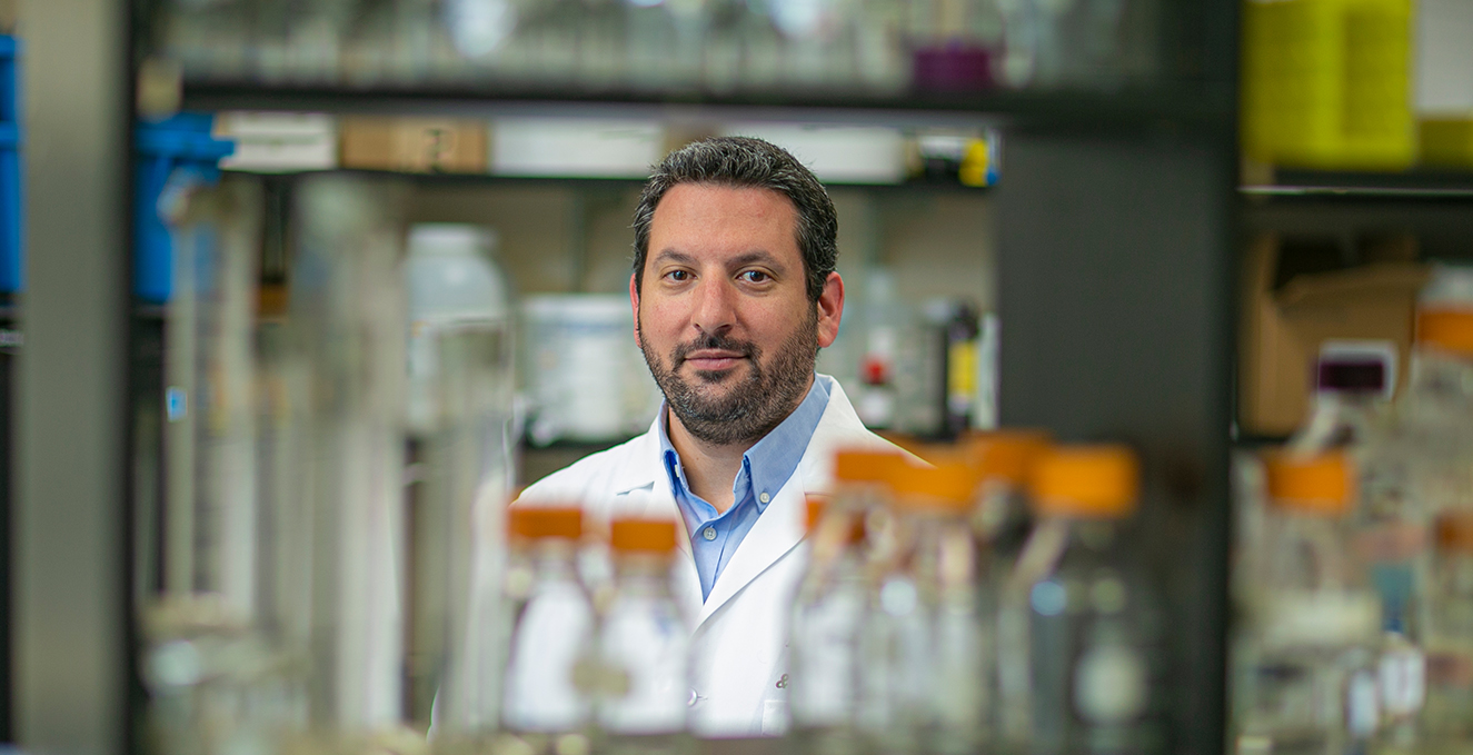 Dr. Manvich smiles at a camera while surrounded by glass bottles in a lab