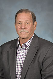Barry Waterhouse smiles at the camera while wearing a plaid button-down shirt and a blazer