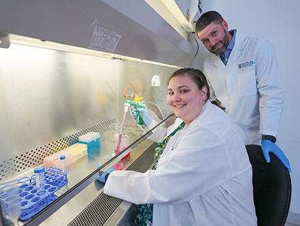 two researchers smile while working under the hood in a lab