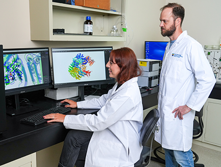 a student researcher looks at an image on a monitor while a faculty research stands behind her